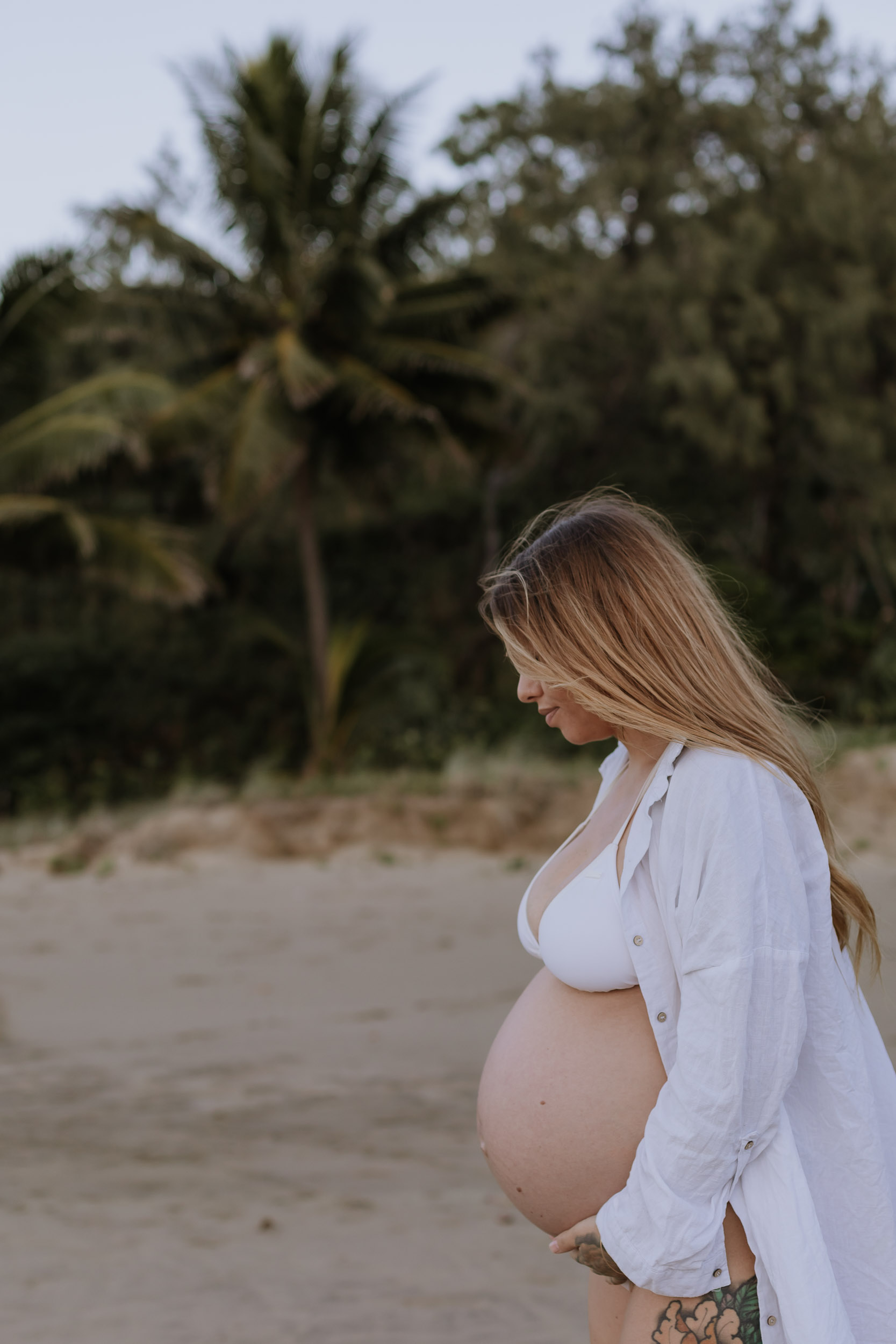 Pregnant woman standing on Mackay beach at sunrise during maternity session