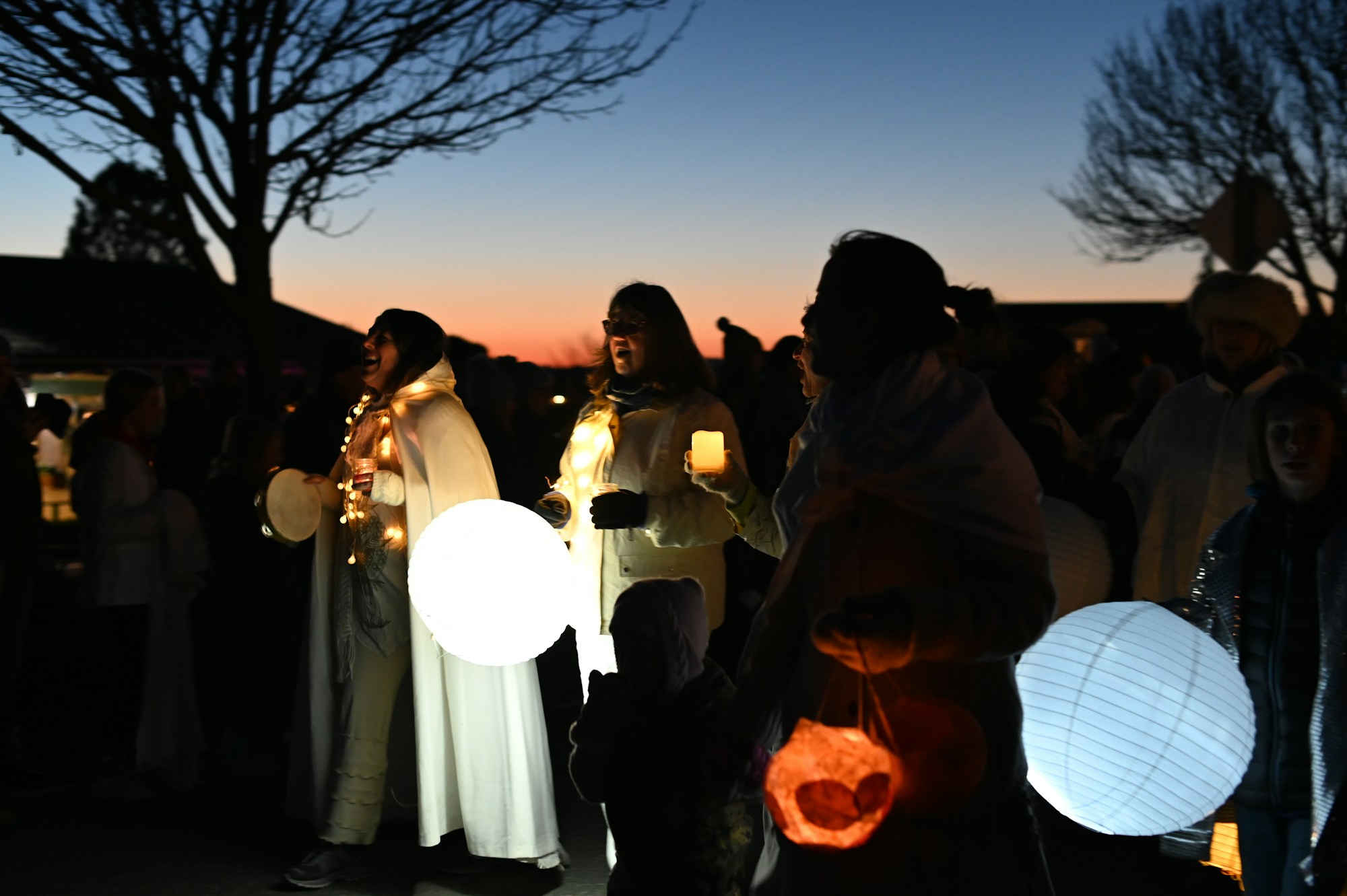 People singing and carrying glowing paper lanterns at dusk