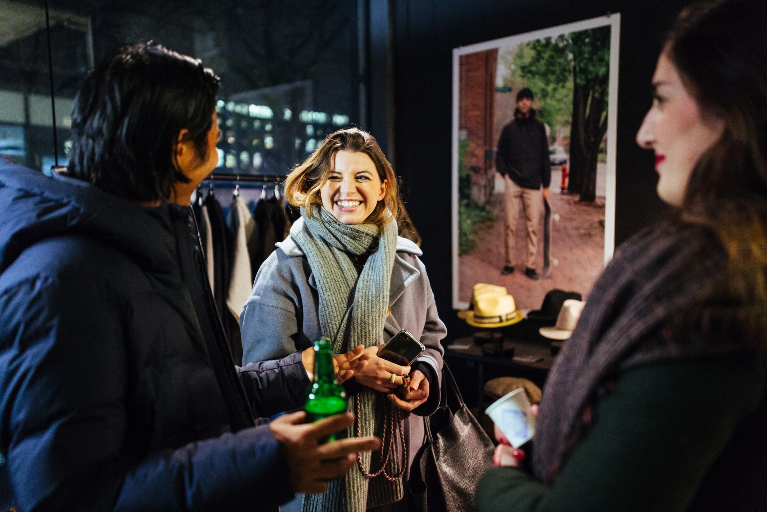 Guests chatting with drinks at the BRIXTON pop-up event in front of a clothing rack, lifestyle posters and a display of hats.