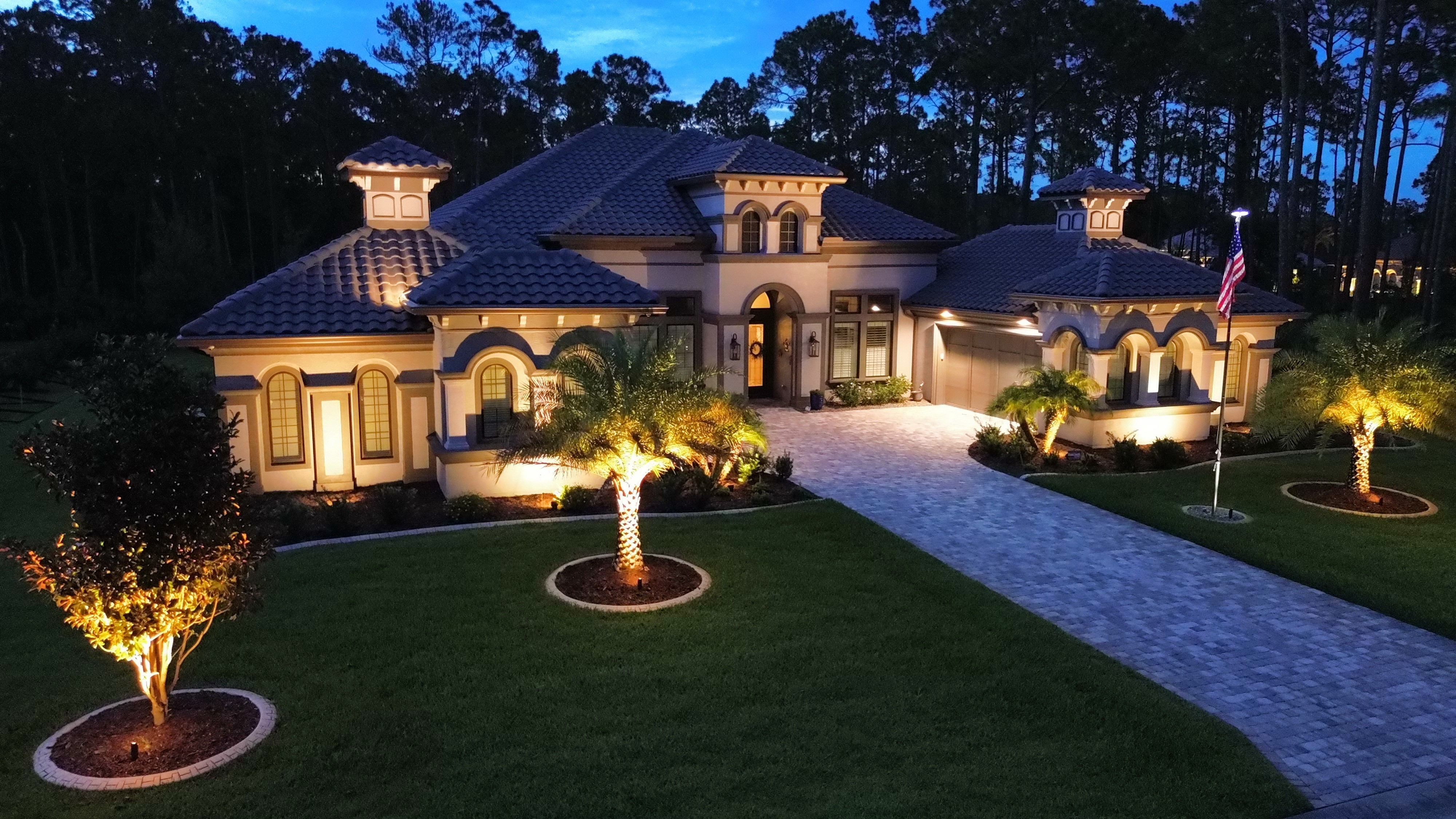 Luxury home with professional landscape lighting illuminating palm trees and front walkway