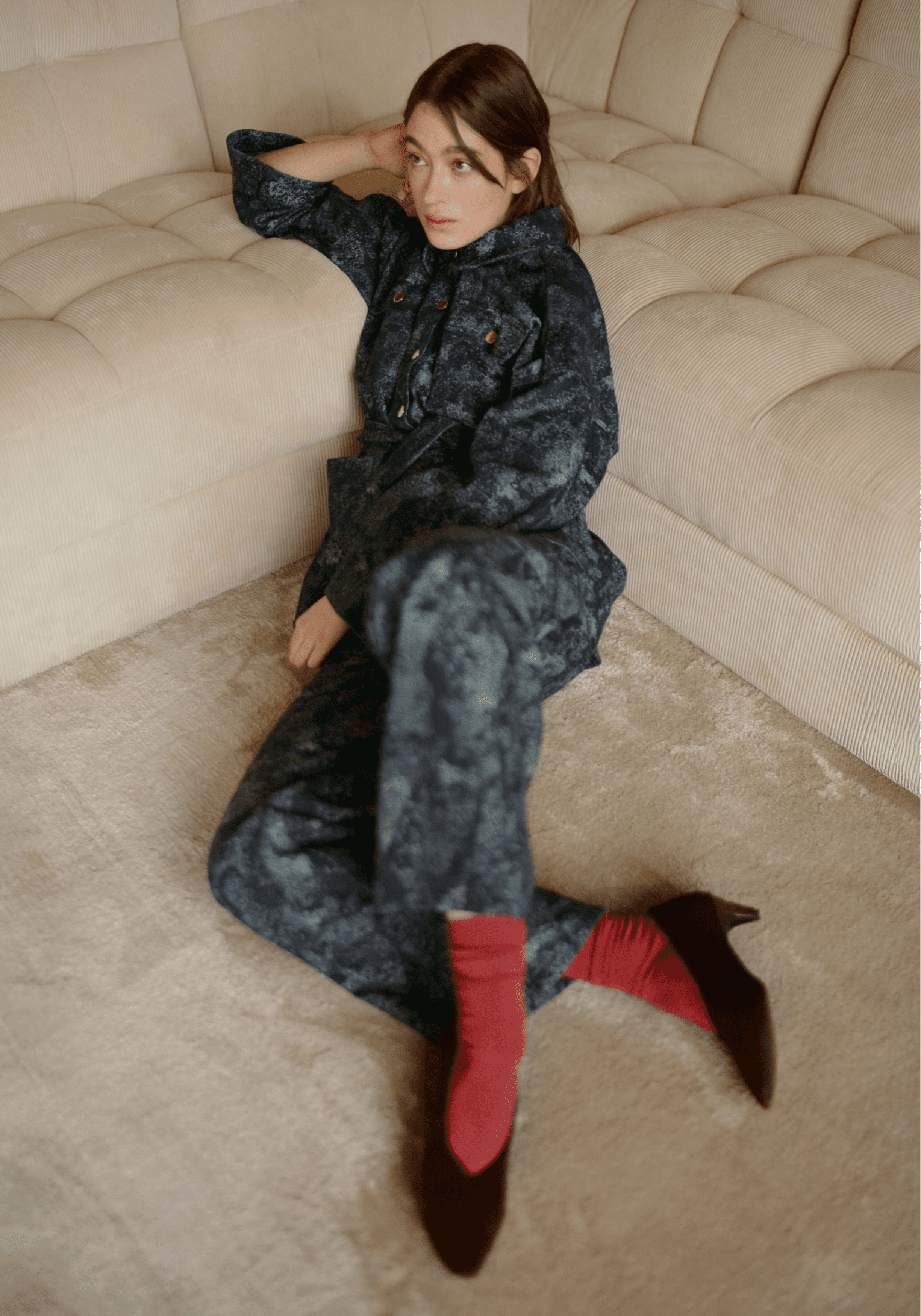 Une femme assise par terre portant un ensemble vert à motif, des escarpins noirs et des chaussettes rouges