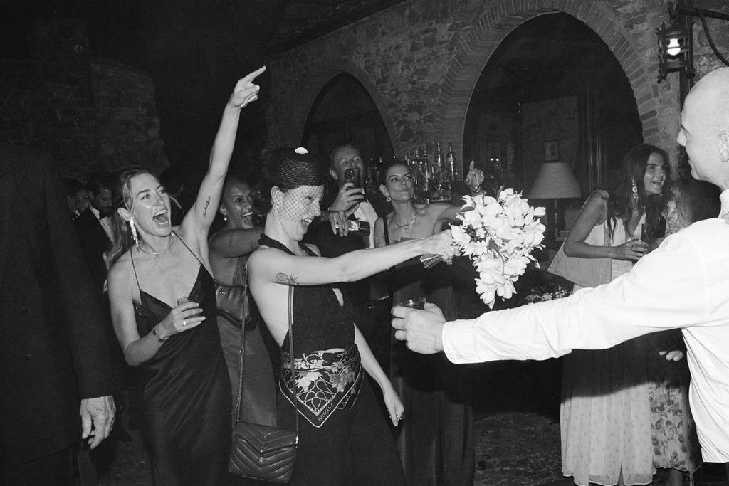 Black-and-white portrait of stylish guest who caught the bride's bouquet and other guests cheering her on