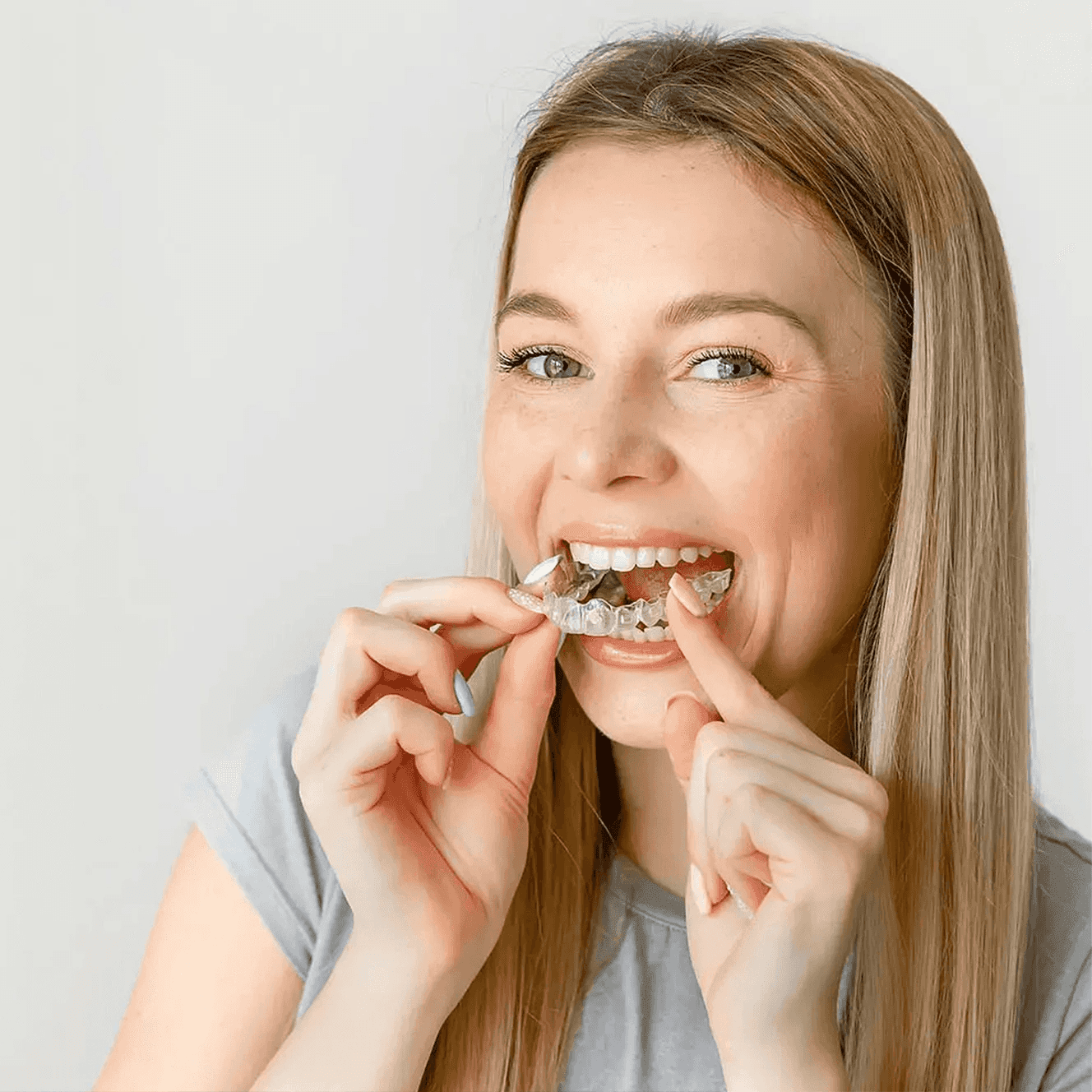 A woman smiles and holds invisalign clear aligners with a case, showcasing a certified invisalign provider at Bella Medical Centre