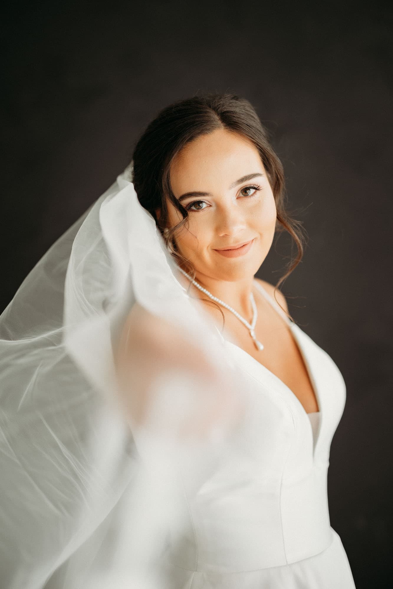 A bride smiles gently while holding her veil, captured in natural light during her bridal session at Revelator Studio, a photography studio in Shreveport.