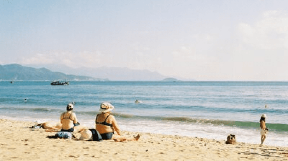 two women in nathing suits sitting on the edge of the beach on a sunny day