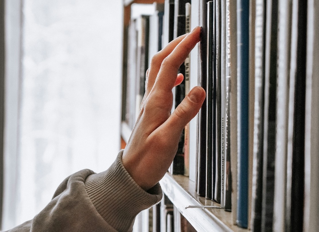 Image of hand searching for a book in the library
