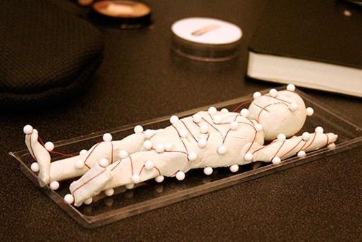 A molded white figurine with small balls all around it and tight by a red wire.