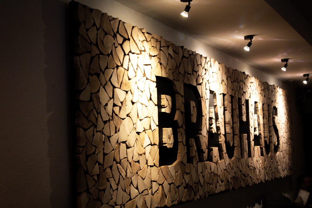 Holzwand mit dem Schriftzug „BRAUHAUS“, beleuchtet durch mehrere Deckenstrahler.
