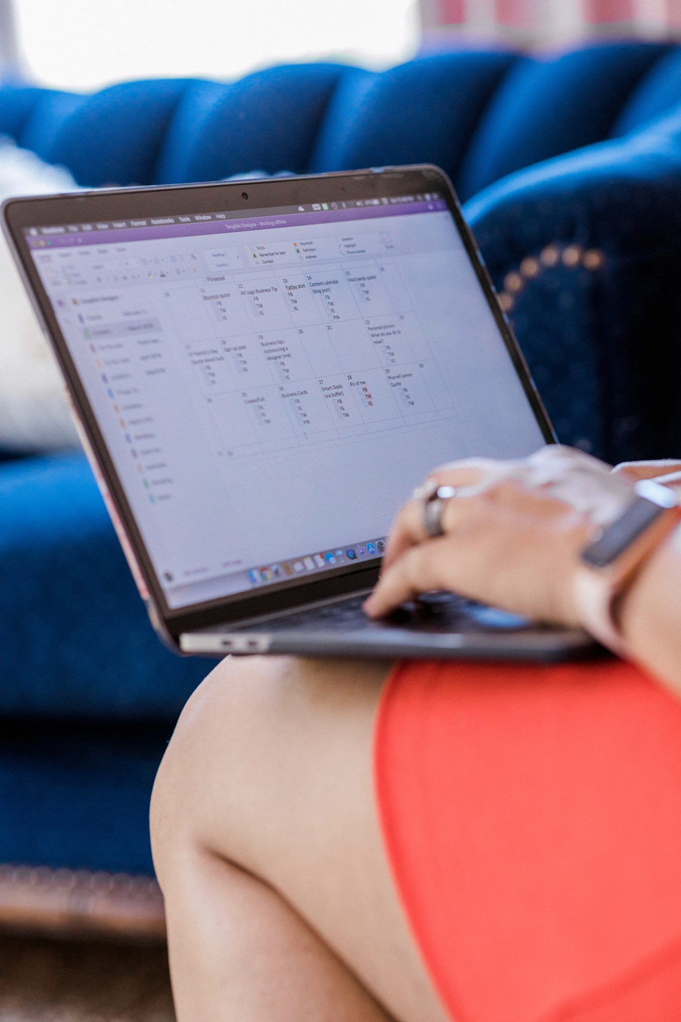 A hand is typing on a MacBook that shows a social media calendar so the user can track their posts