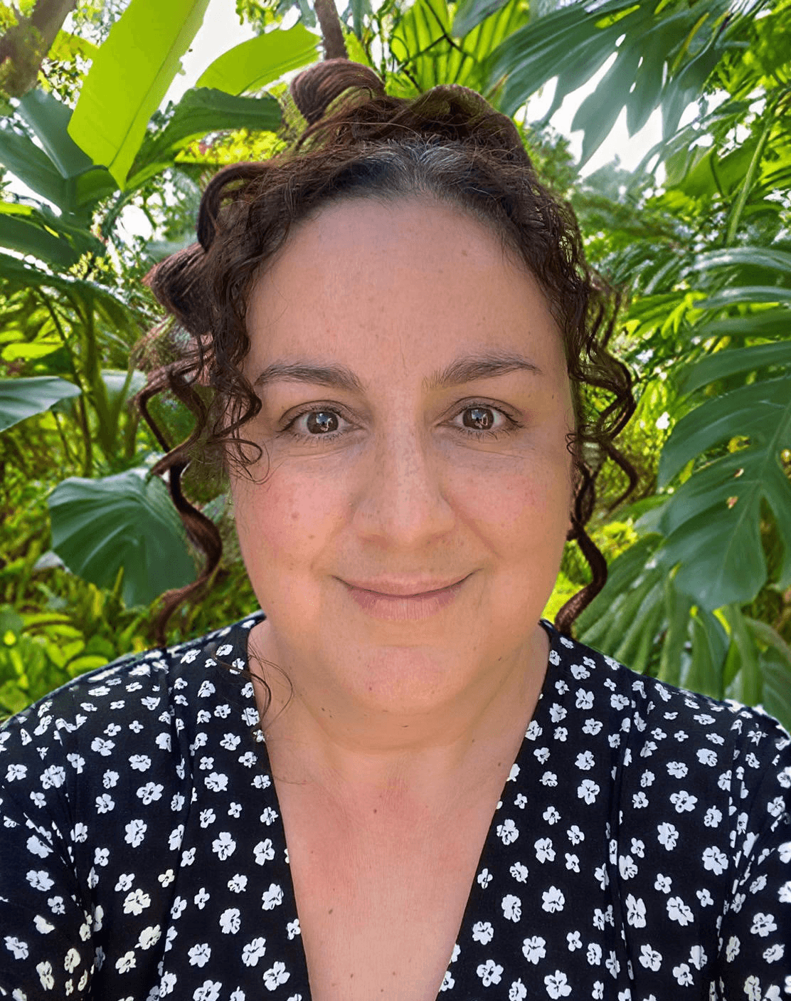 Smiling female therapist with short gray hair, wearing a brown top and a purple shawl, surrounded by a cozy background.