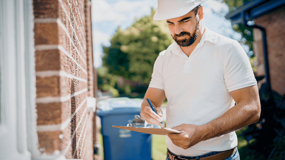 Property inspector completing documentation on a clipboard during an exterior home inspection.