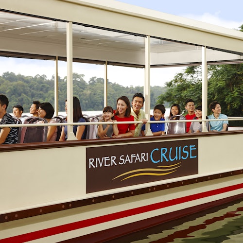 家庭们坐在标有“河流探险游轮”的开放式游船上微笑,背景是茂密的森林。