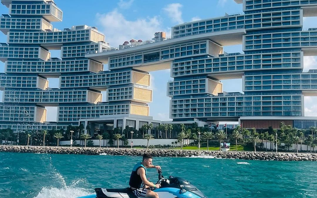 A person riding a jet ski near a modern architectural building with stacked rectangular structures; ideal for learning jet ski tips and tricks while enjoying scenic views