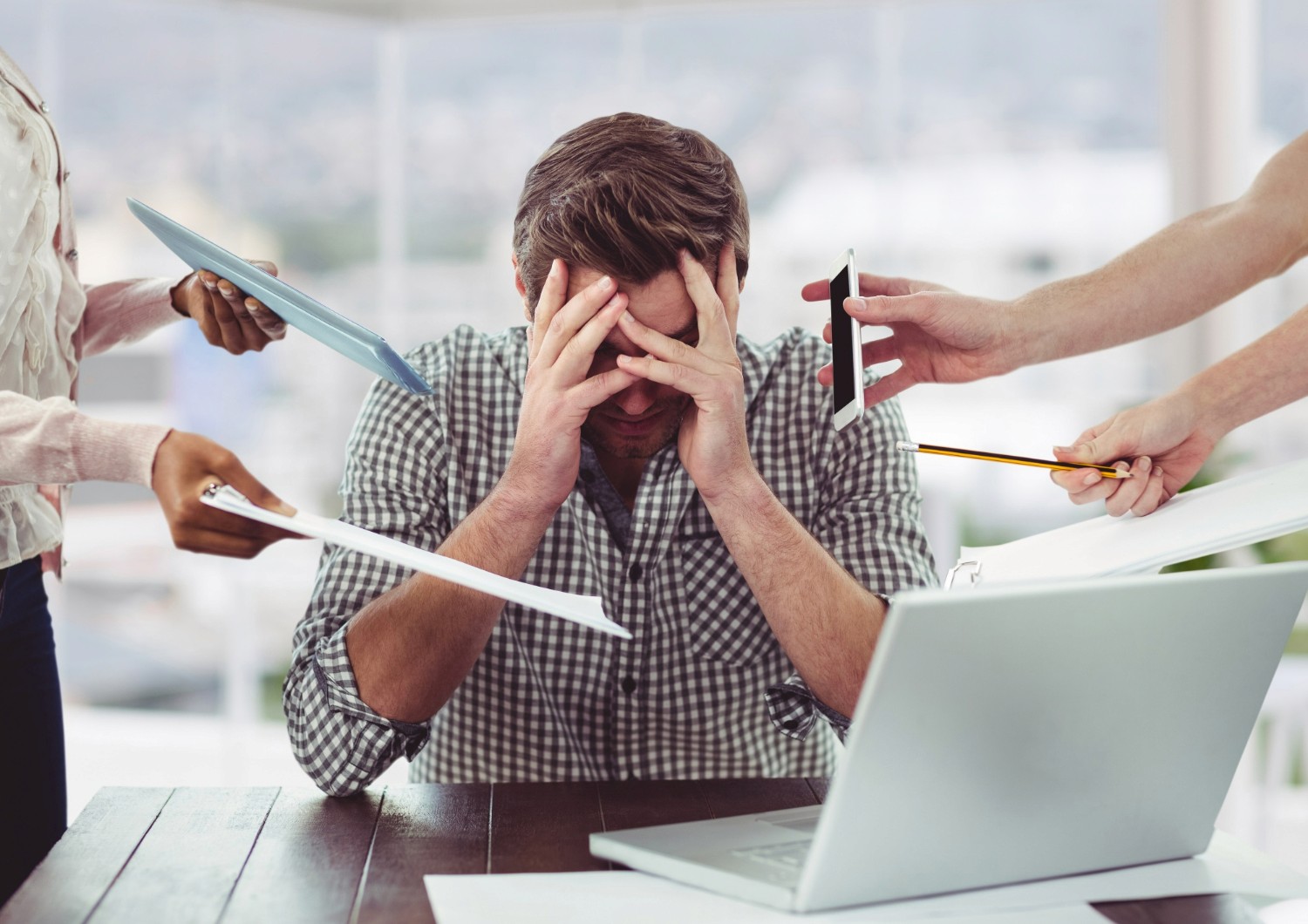 Profissional com as mãos no rosto em mesa de trabalho com papelada e outras pessoas solicitando demandas