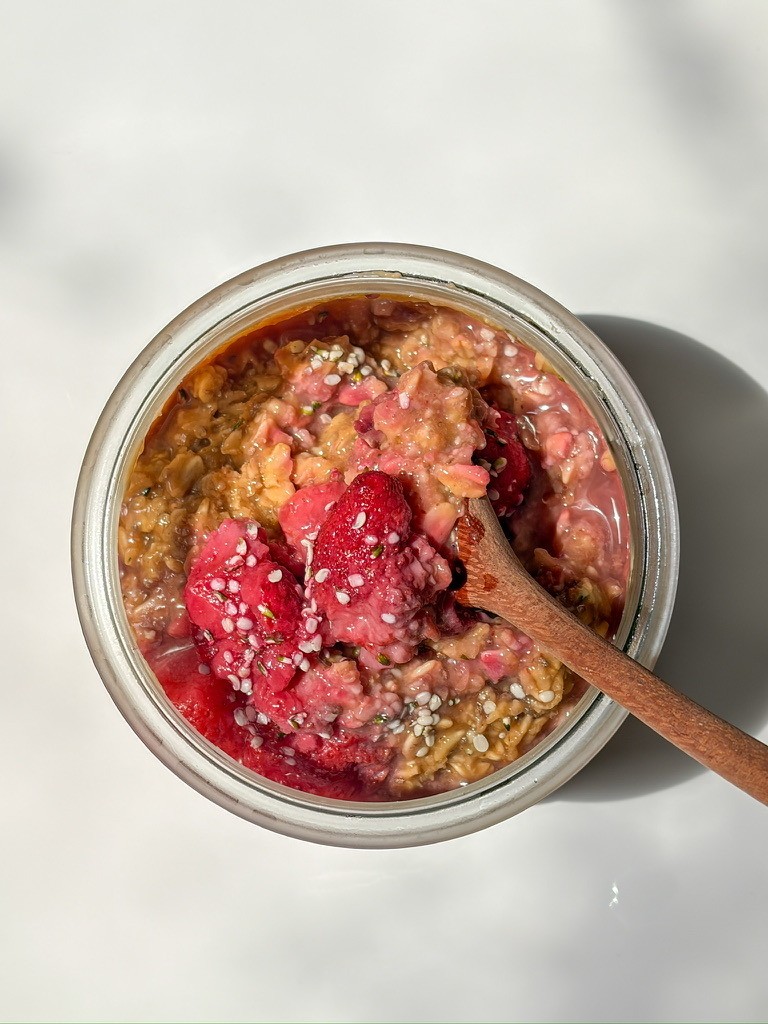 high-protein peanut butter & strawberry jelly overnight oats in a glass container with a wooden spoon