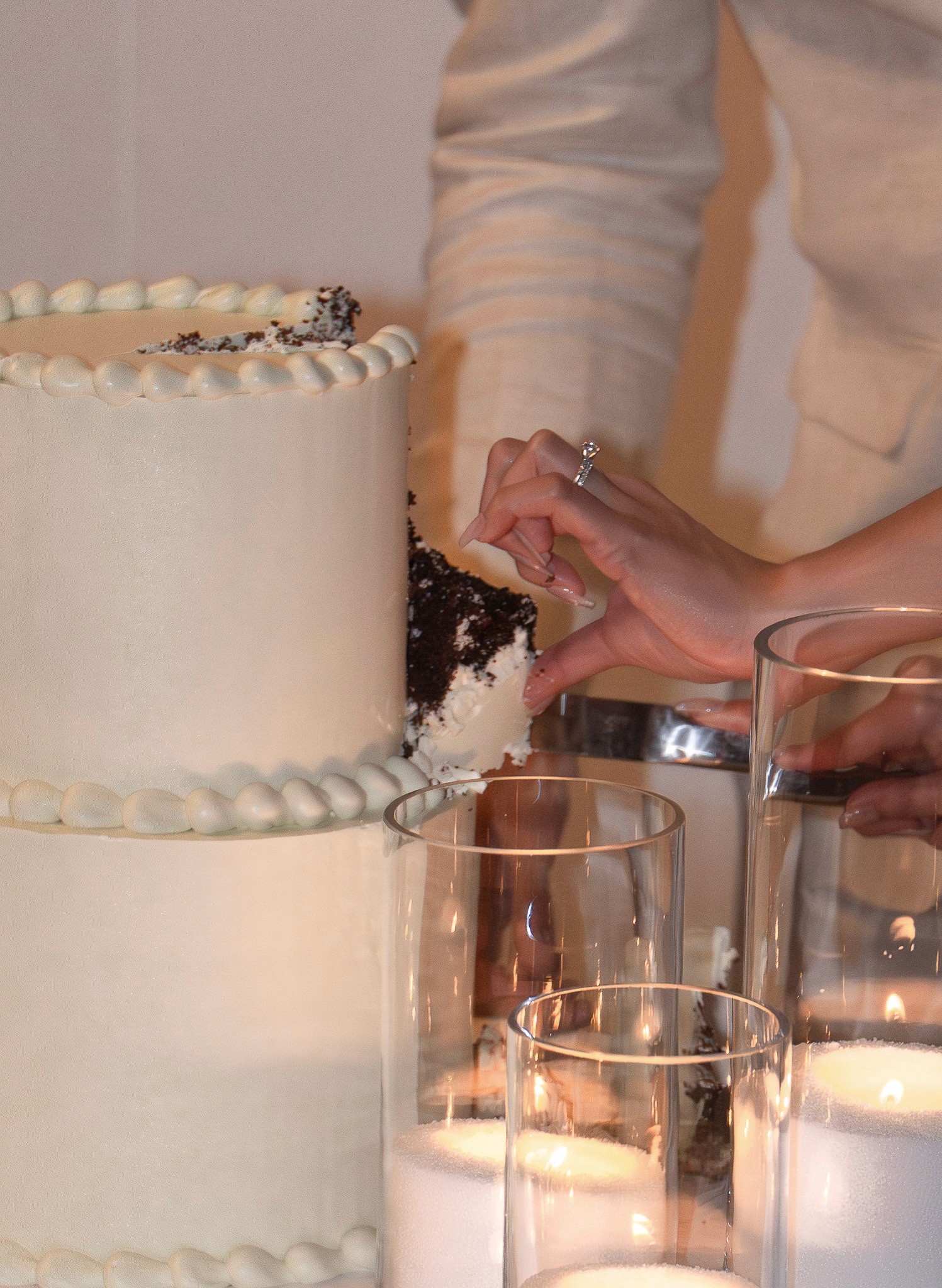 Close-up of a couple cutting a white wedding cake beside candlelit glasses.