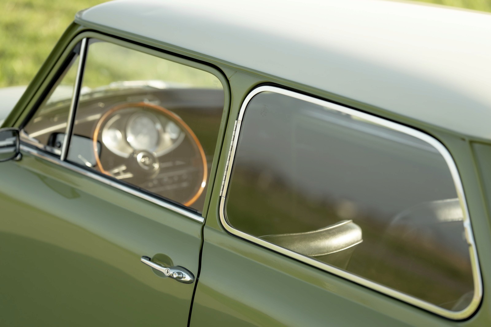 Close-up of a green vintage car's open window, revealing the steering wheel and interior details.