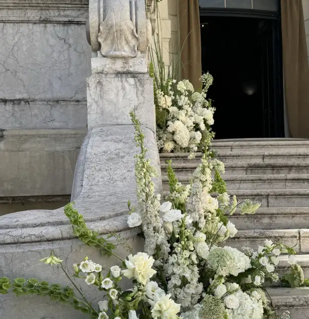 Instalación floral en tonos blancos y verdes sobre escalinata de mármol para evento institucional o ceremonia elegante, resaltando pureza y solemnidad.