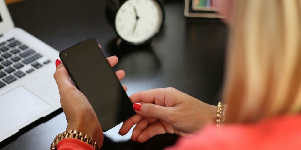 woman sitting holding smartphone near laptop