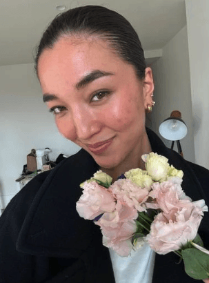 A woman lying down in a spa setting, relaxing with her eyes closed. Sunlight streams through blinds, casting striped shadows on her face. The scene conveys a sense of serenity and well-being.