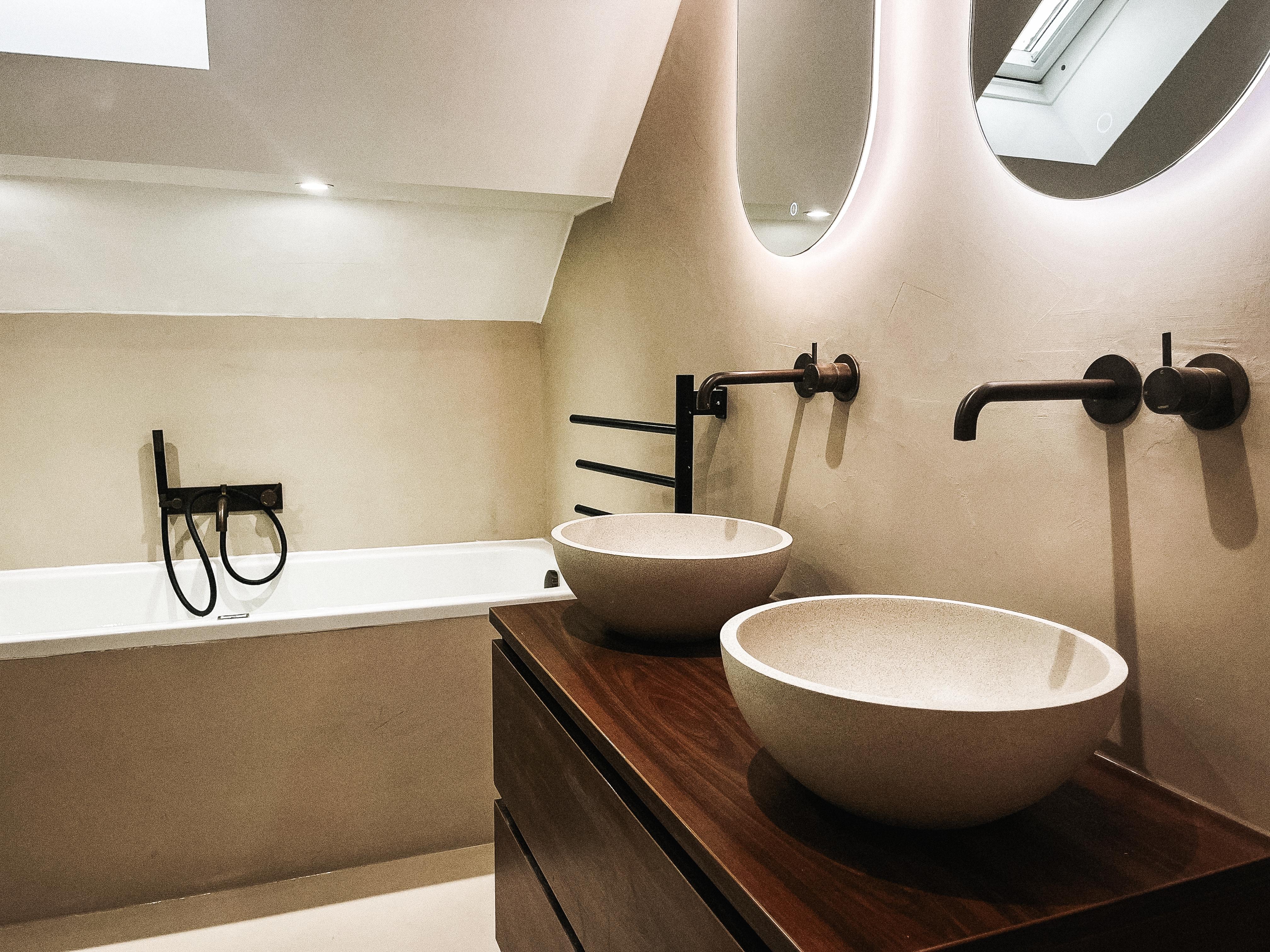 Stijlvolle en moderne badkamer met inloopdouche, dubbele wastafel, beton cire vloer en wand. De badkamer heeft een minimalistisch ontwerp met strakke lijnen, grote spiegels met lamp en luxe afwerkingen voor een eigentijdse uitstraling.