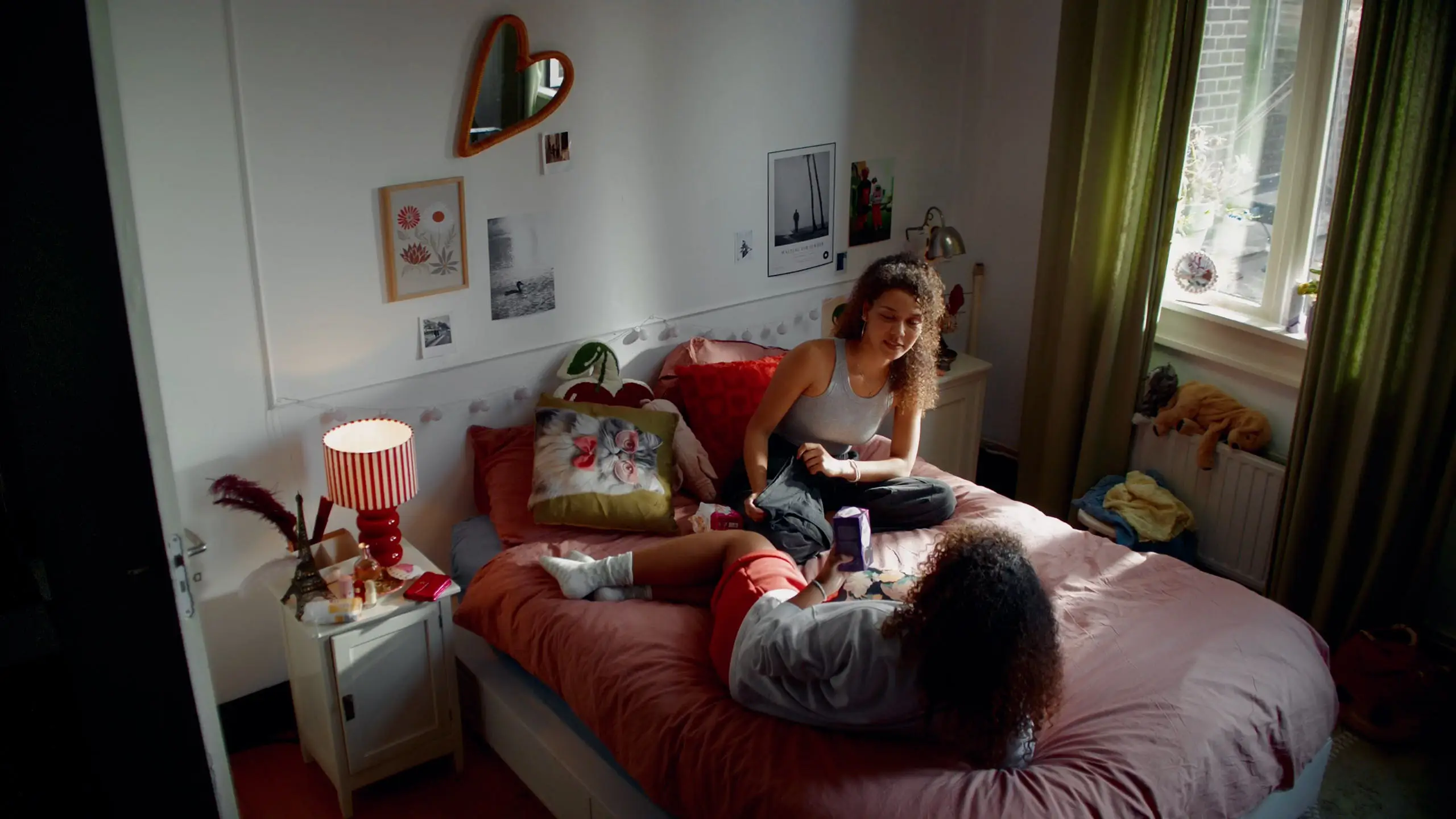 Wide shot of two sisters sitting and lying on a bed in a cosy, personal bedroom.