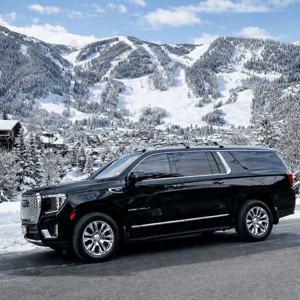 Luxury black SUV providing transportation from Denver to Aspen during winter, with Aspen village and snow-covered mountains in the background.