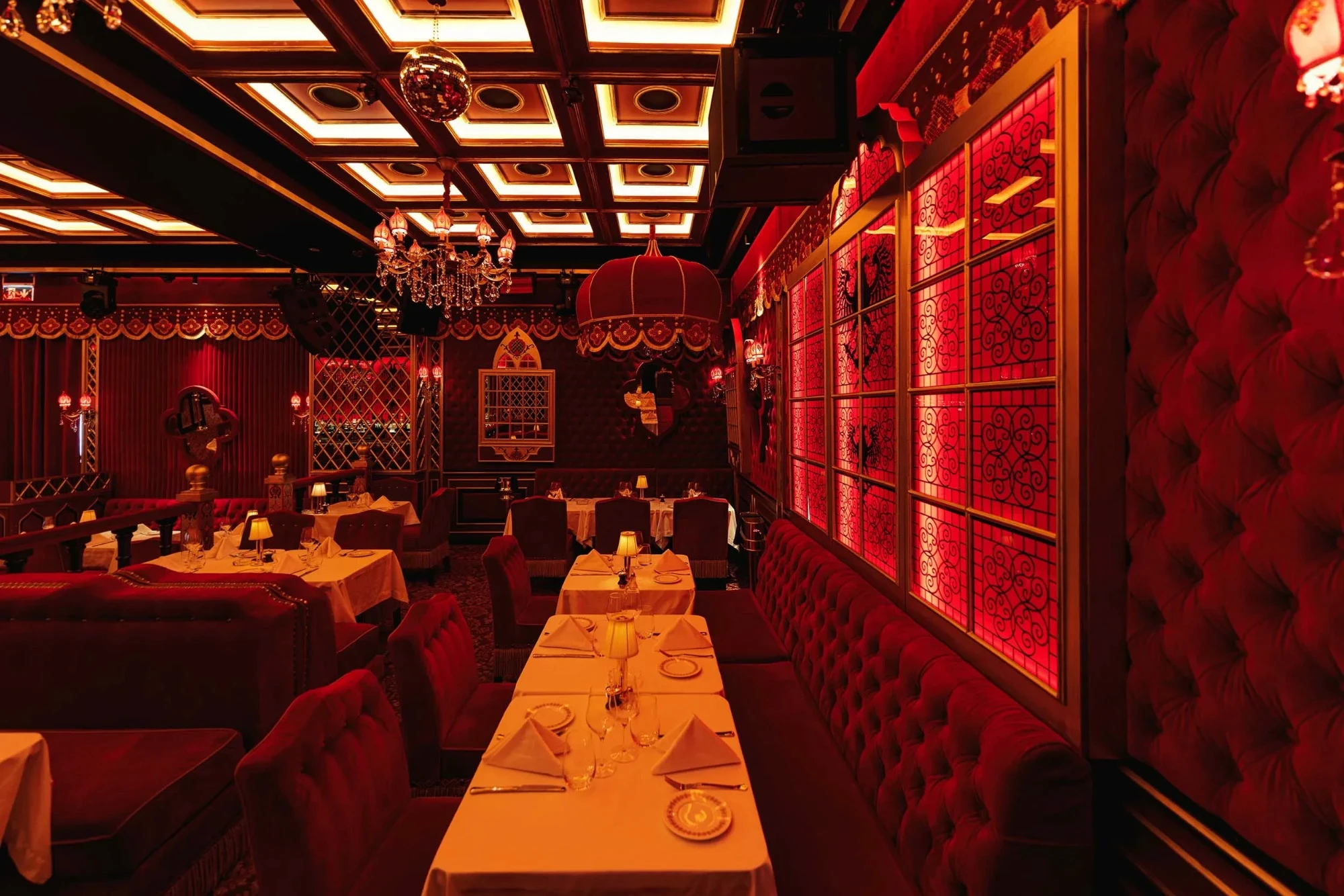Raspoutine Dubai dining room with red tufted velvet banquettes, white tablecloths, table lamps and crystal chandeliers