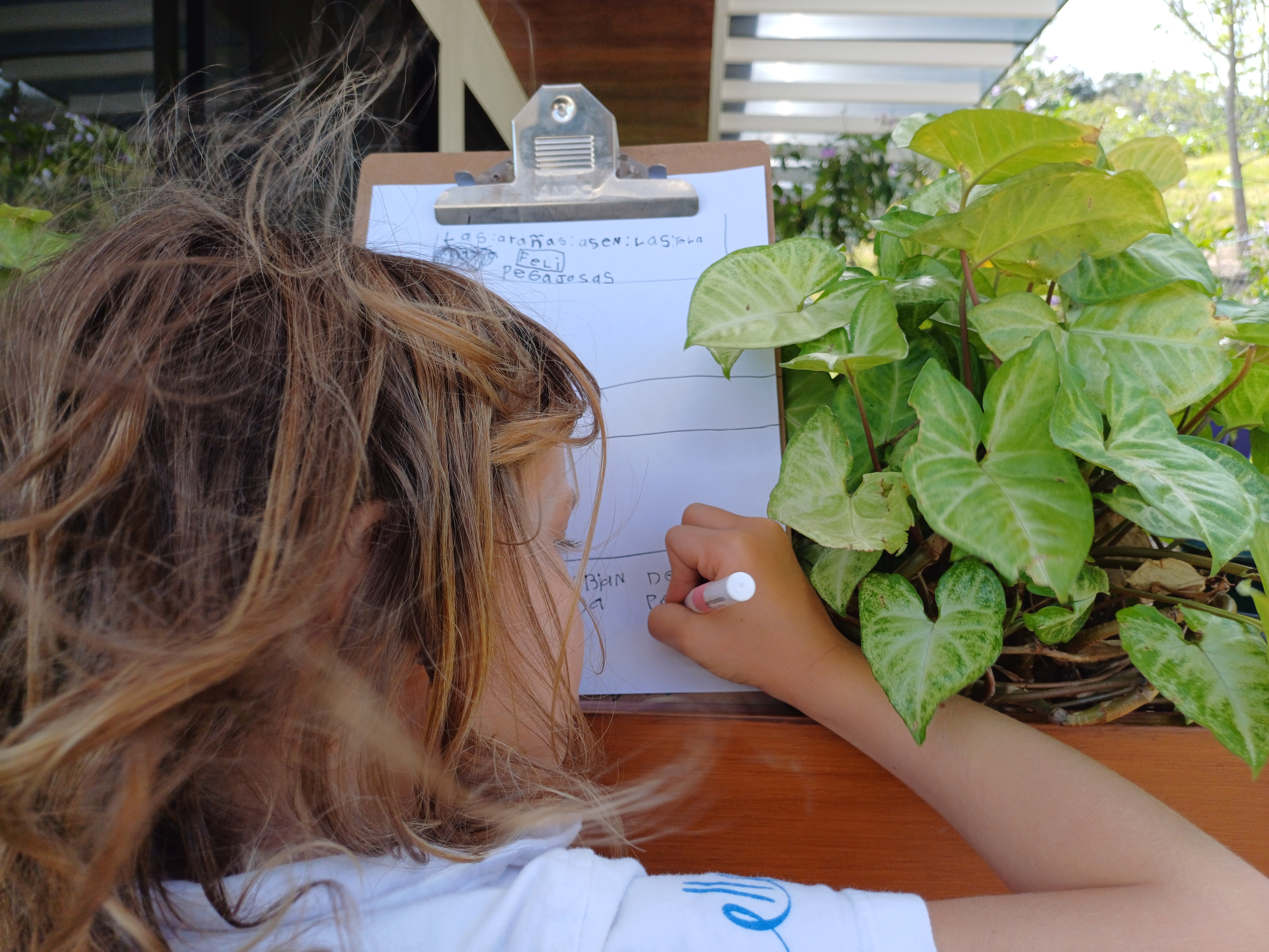 Estudiante escribiendo notas en un portapapeles junto a plantas, representando la observación y la investigación científica