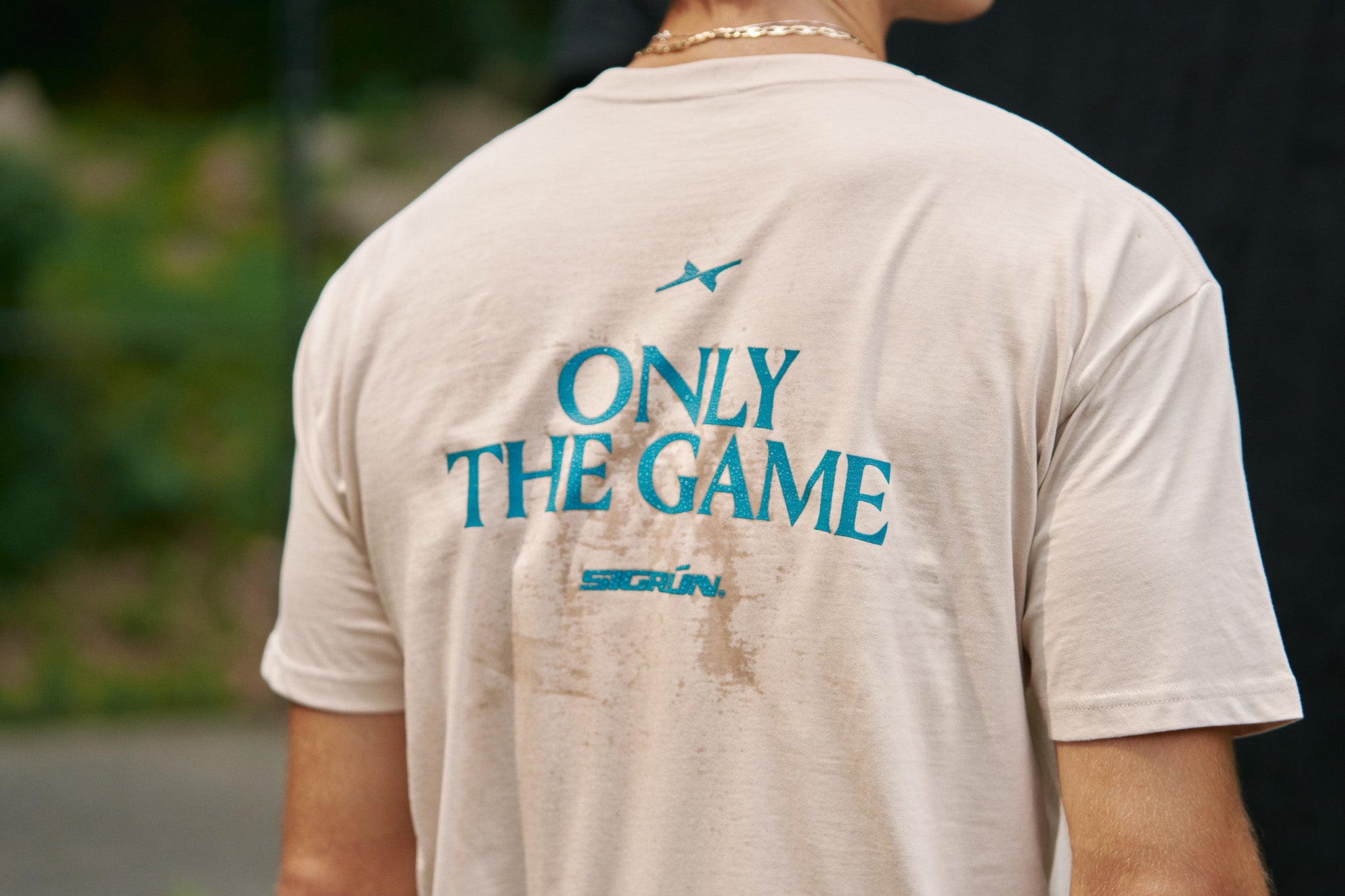 Back of a cream Sigrún T-shirt with turquoise Only the Game lettering.