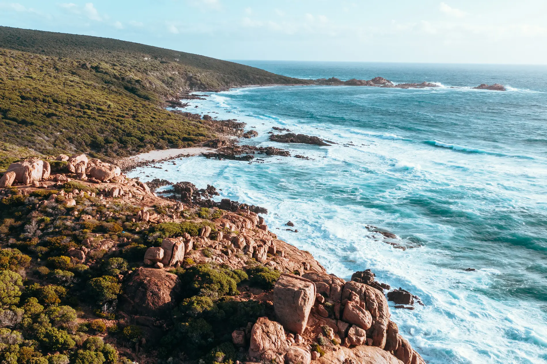 Aerial of a rocky coastline with surf breaking below scrub-covered slopes