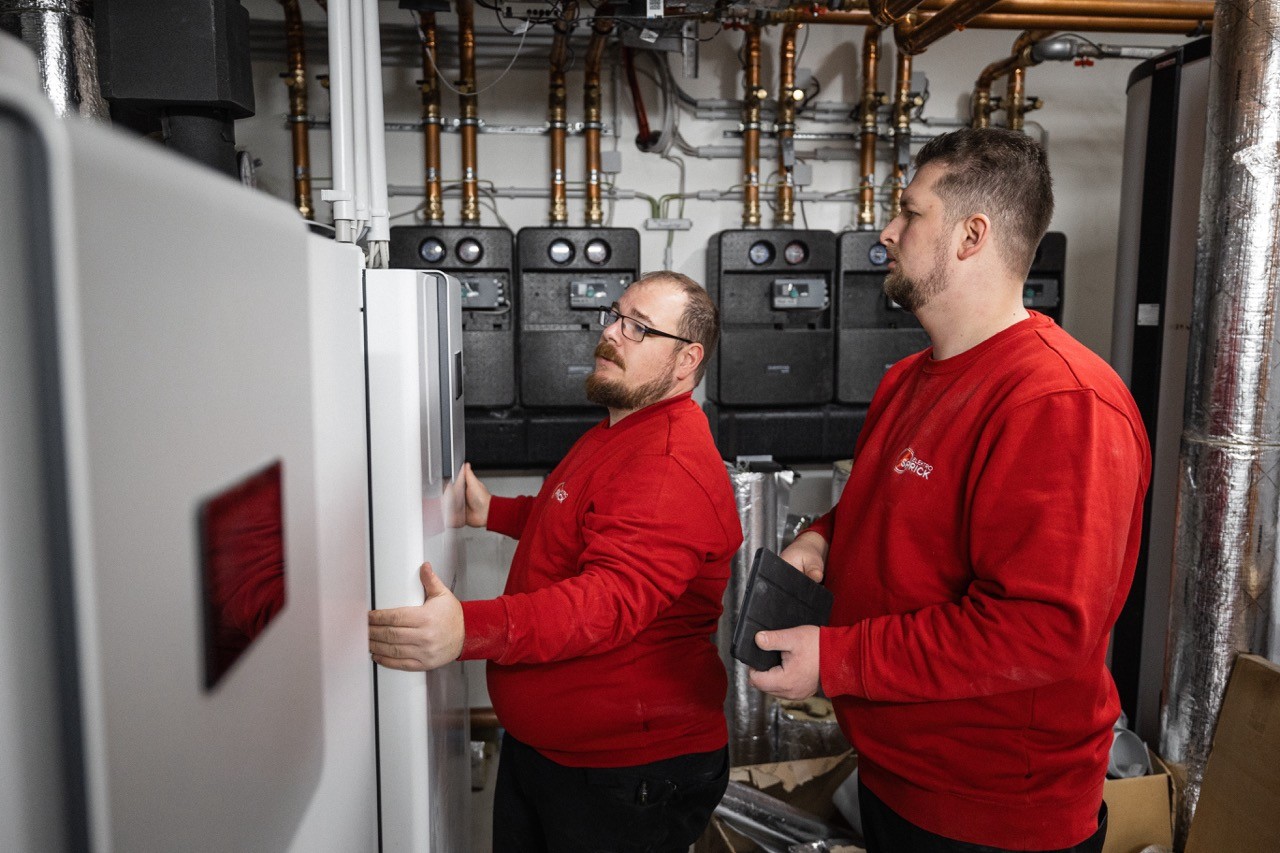 Zwei Installateure in roter Arbeitskleidung montieren eine Wärmepumpe im Heizungskeller.