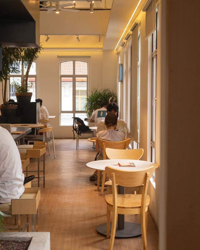 Interior view of 103 Coffee café, showing wooden furniture, patrons seated at tables, and large windows allowing natural light to fill the space.