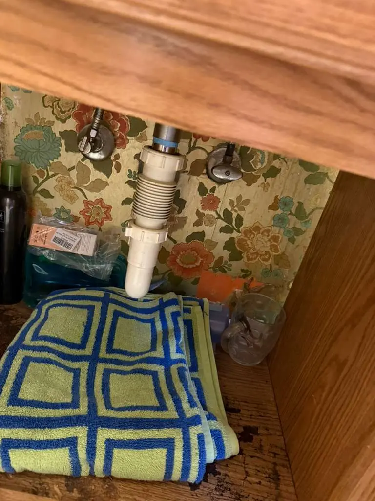 A disconnected sink drain pipe leaking onto a towel inside a bathroom cabinet, requiring professional water leak repair.