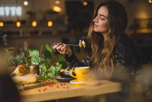 Woman enjoying a healthy meal with vegetables and tea in a softly lit kitchen.