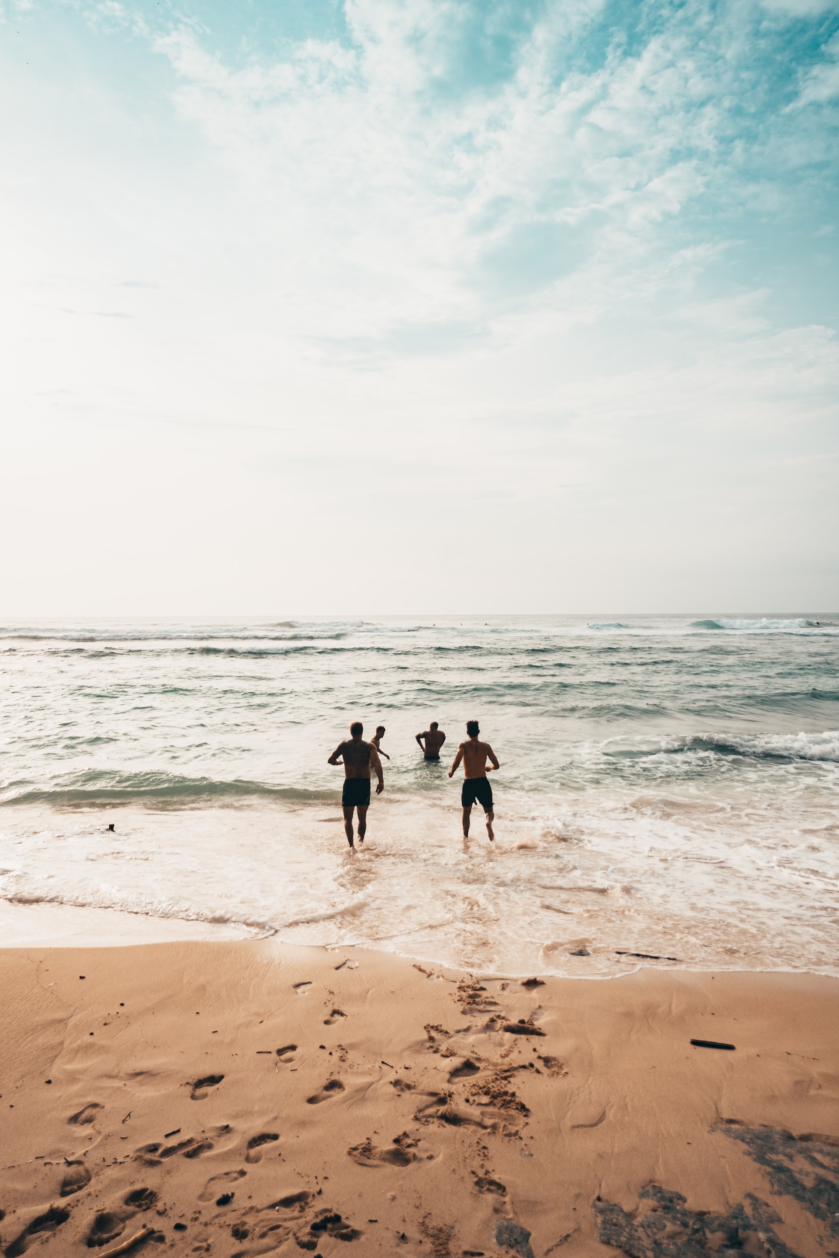 3 friends running from the beach into the sea waves.