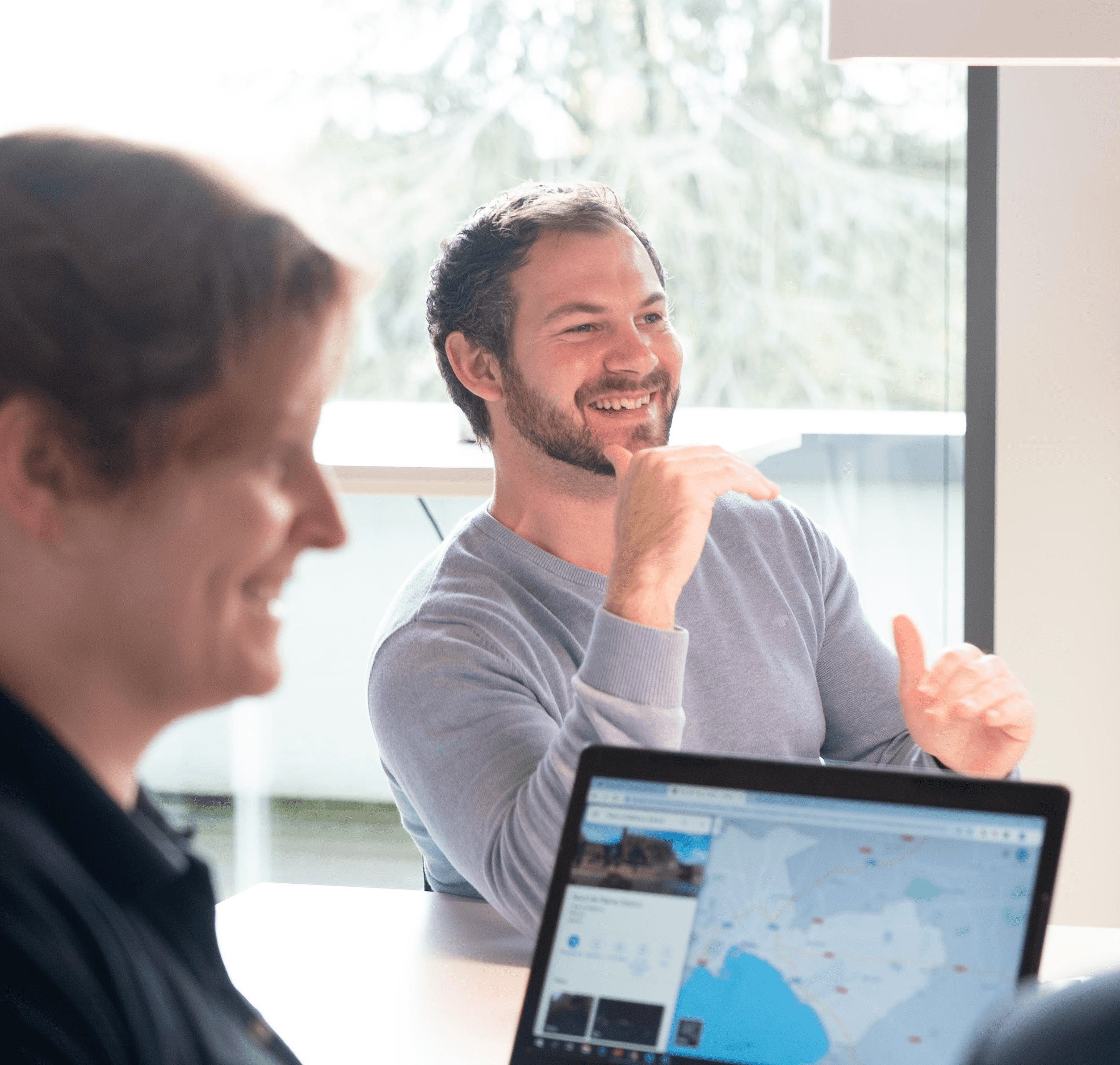 Mann lächelt während einer Teamdiskussion mit Laptop auf dem Tisch.