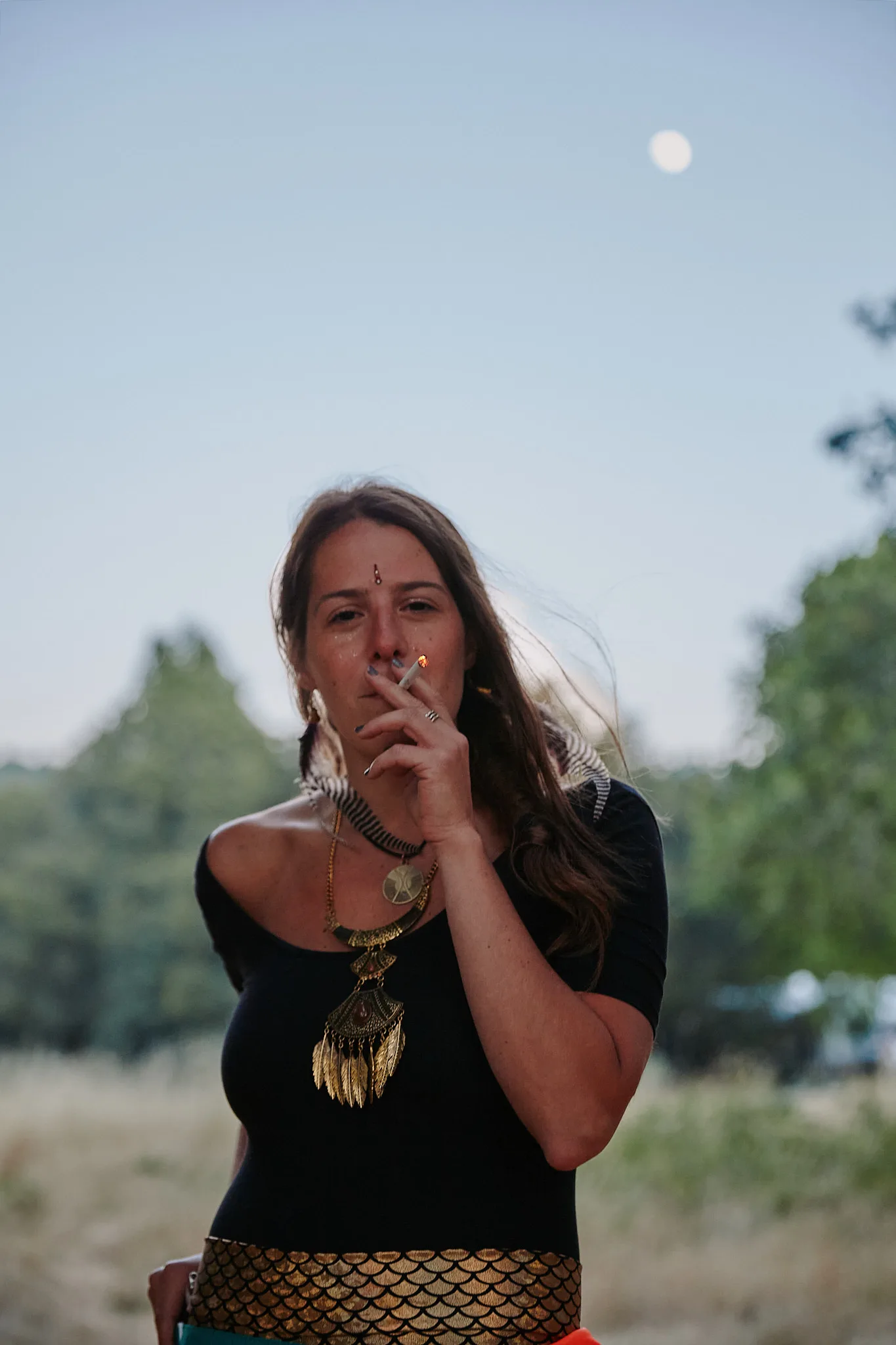 woman lighting cigarette under daytime moon — portrait photography by Tom Kubik