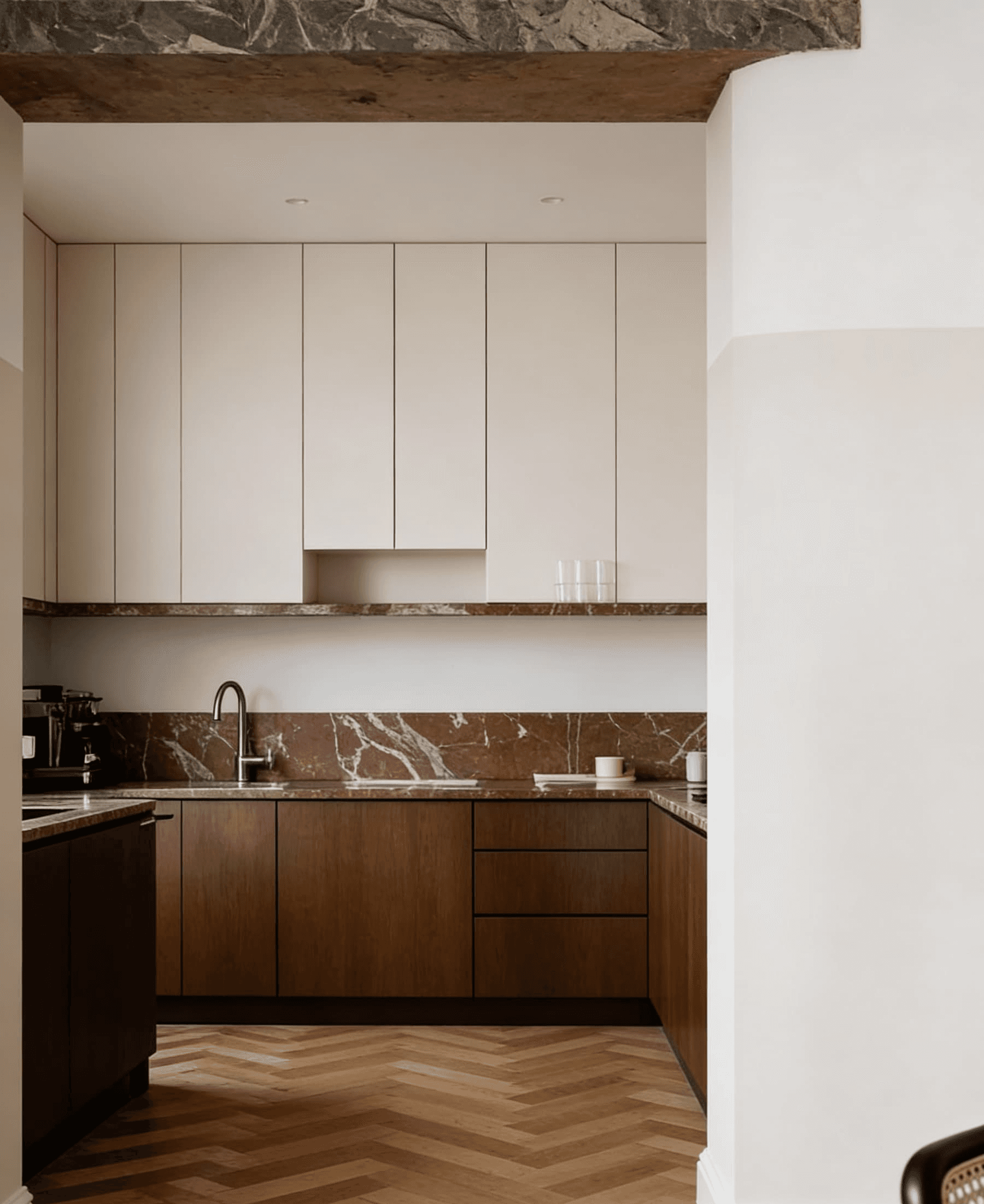 A modern kitchen featuring sleek, white cabinetry, a marble backsplash, warm wooden lower cabinets, and a stylish herringbone-patterned floor, creating an elegant and functional cooking space.