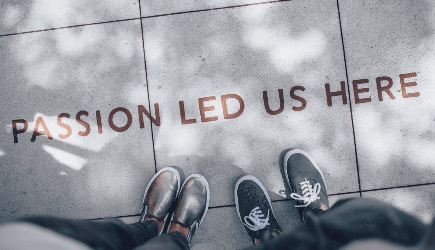 A pair of shoes is seen from above, with the words "Passion Led Us Here" displayed on the ground below.