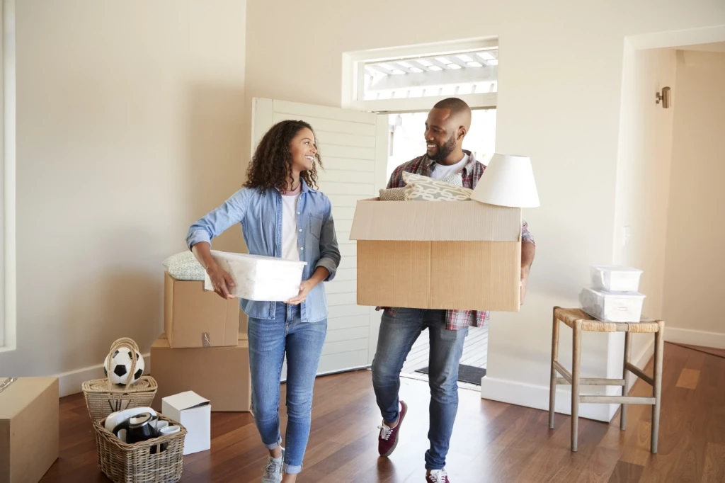 Happy young couple holding boxes moving into new home smiling at each other.