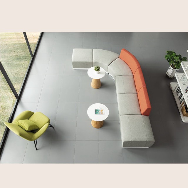 L-shaped modular sectional sofa in light gray with orange backrests, paired with a lime green accent chair and wooden pedestal side tables in a bright, modern office interior.