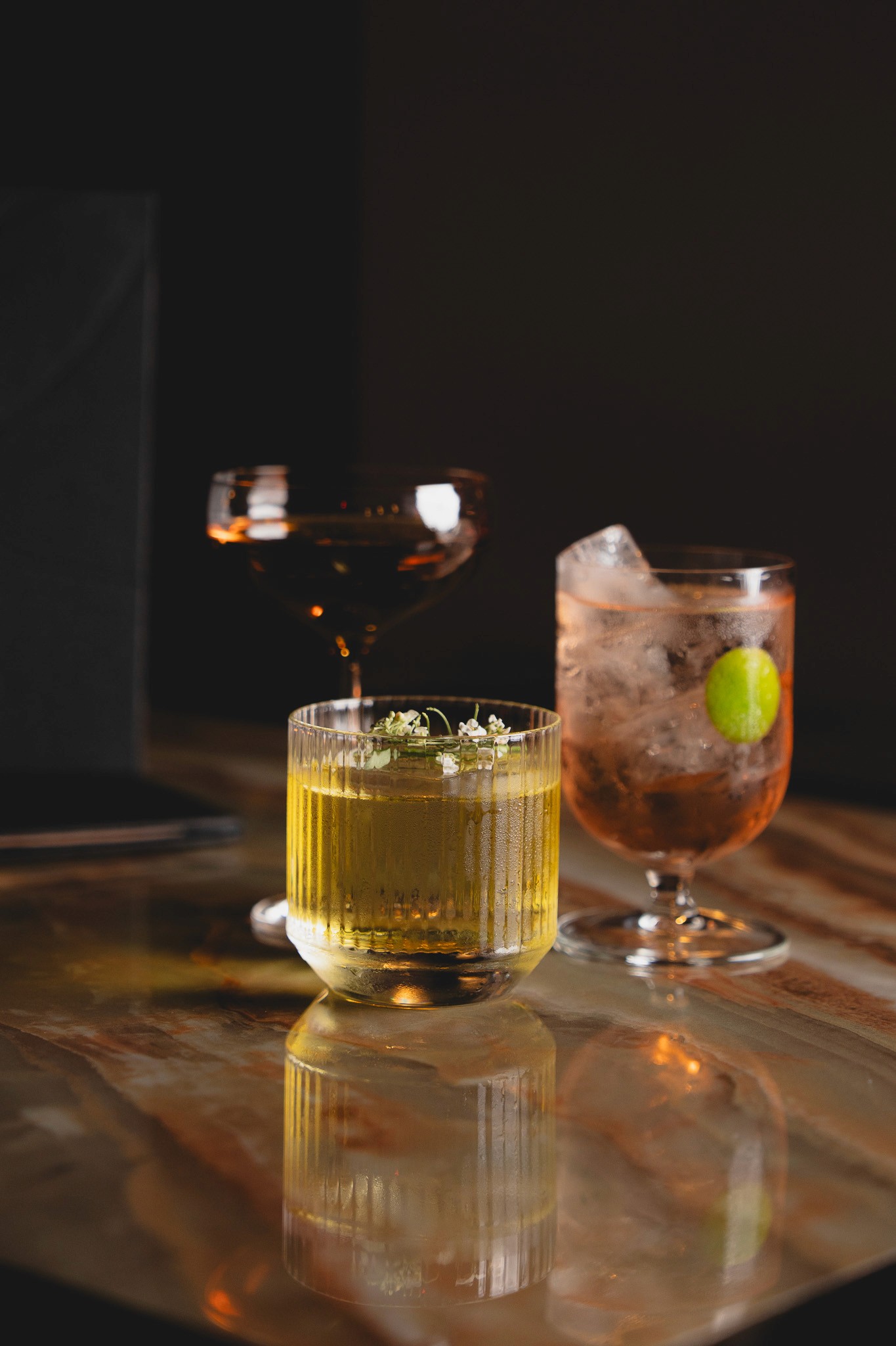 Wooden outdoor table set with multiple plates of food, including dips, salads, potatoes with cheese, and glasses of water, with hands reaching in to eat.