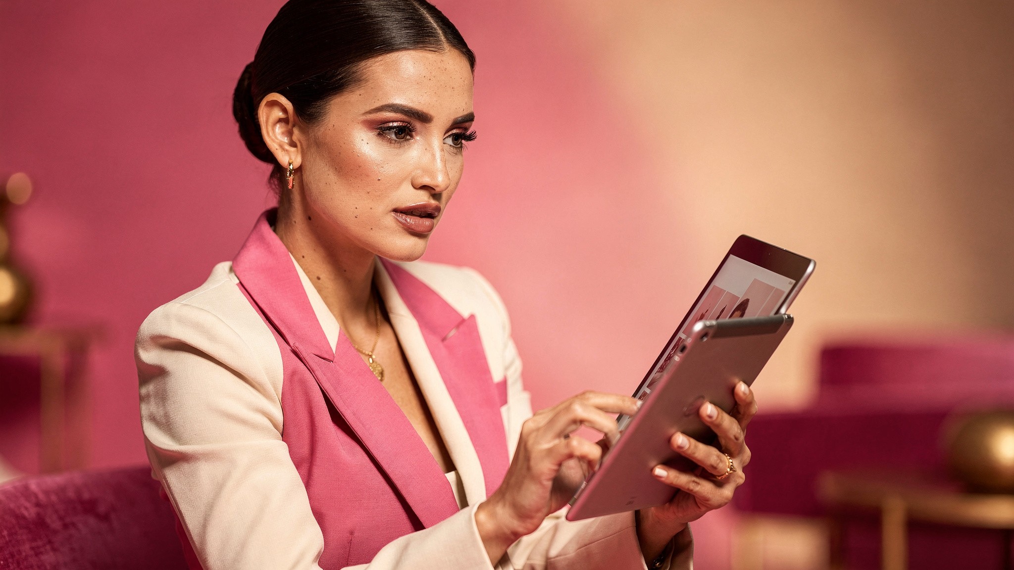 Adult creator reviewing carousel slide designs on a tablet in a bright pink studio