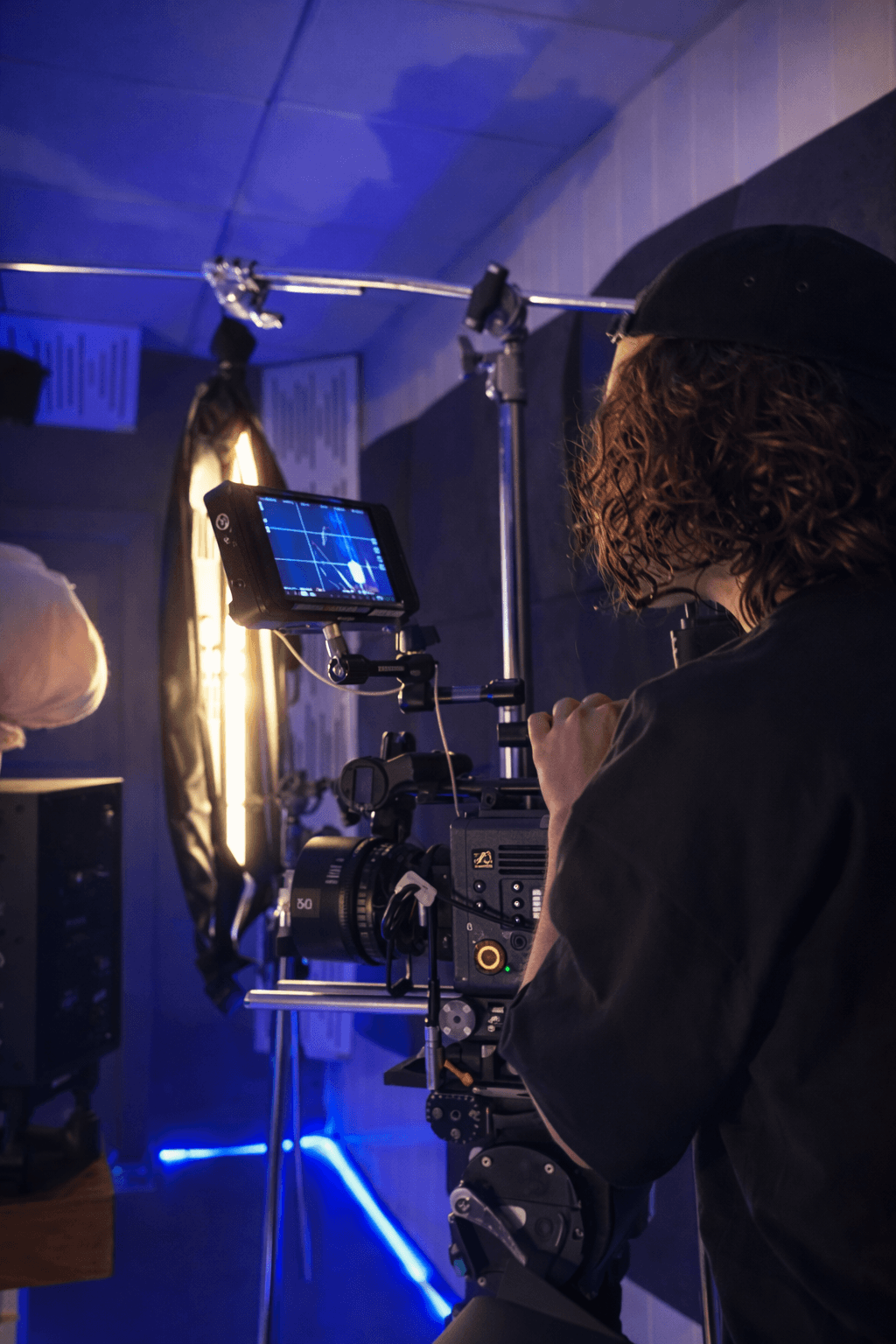 A woman stands beside an old projector, gazing at the camera. The scene is lit with teal and red hues, creating a mysterious and artistic atmosphere.