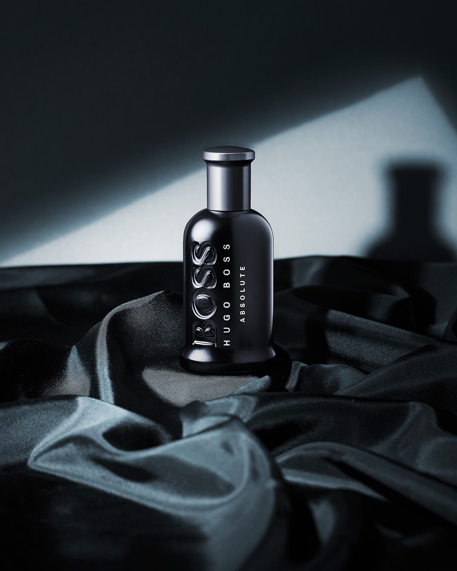 A glass bottle sits on a dark surface, surrounded by various objects, illuminated by a soft light source.