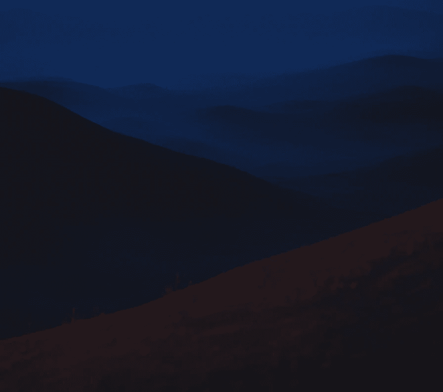 Dark atmospheric landscape at night with layered rolling hills, a deep blue sky, and a subtle warm amber glow along the foreground ridge.