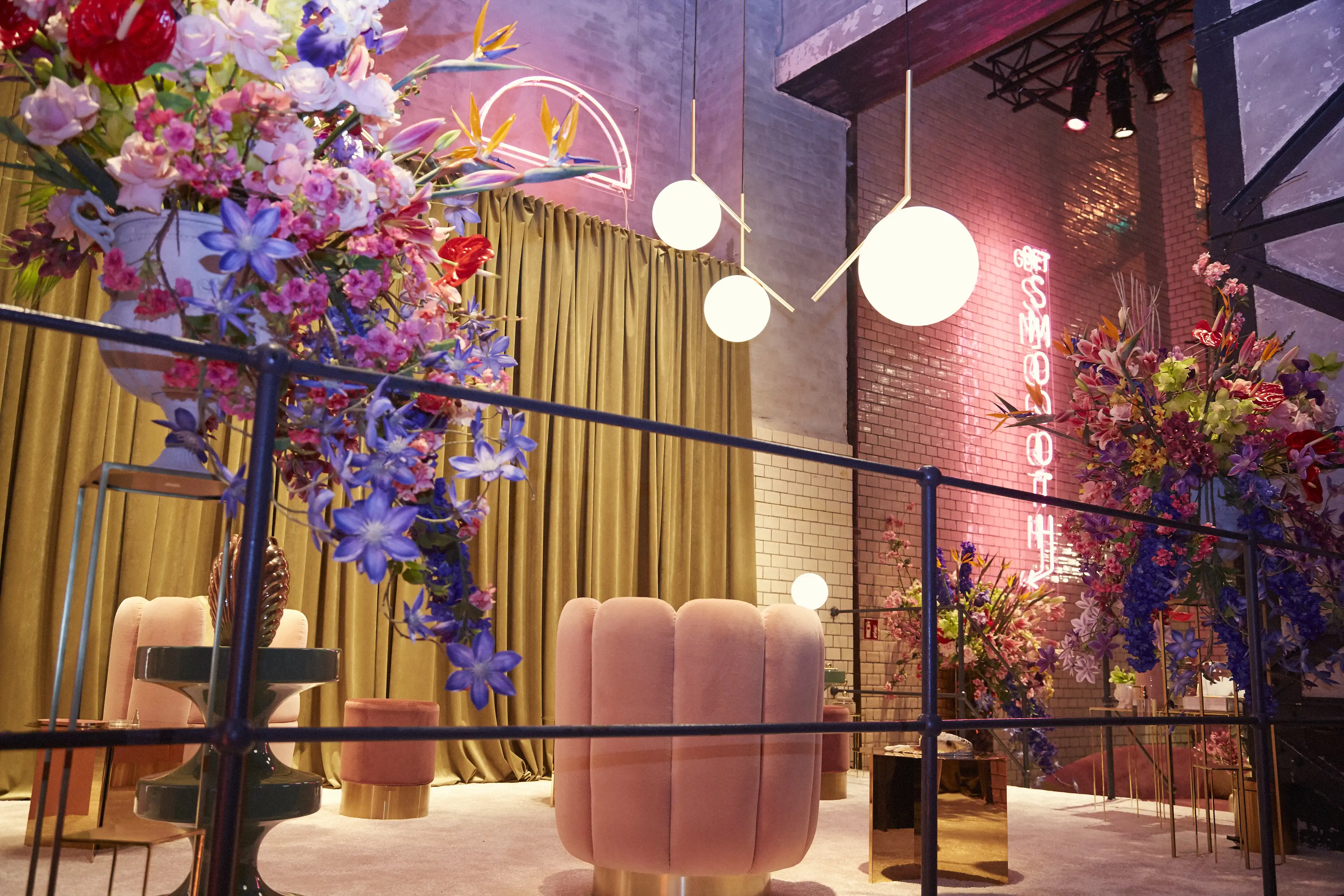 Pink velvet poufs and globe pendant lights in front of gold curtains and a neon-lit brick wall at the Klarna pop-up.