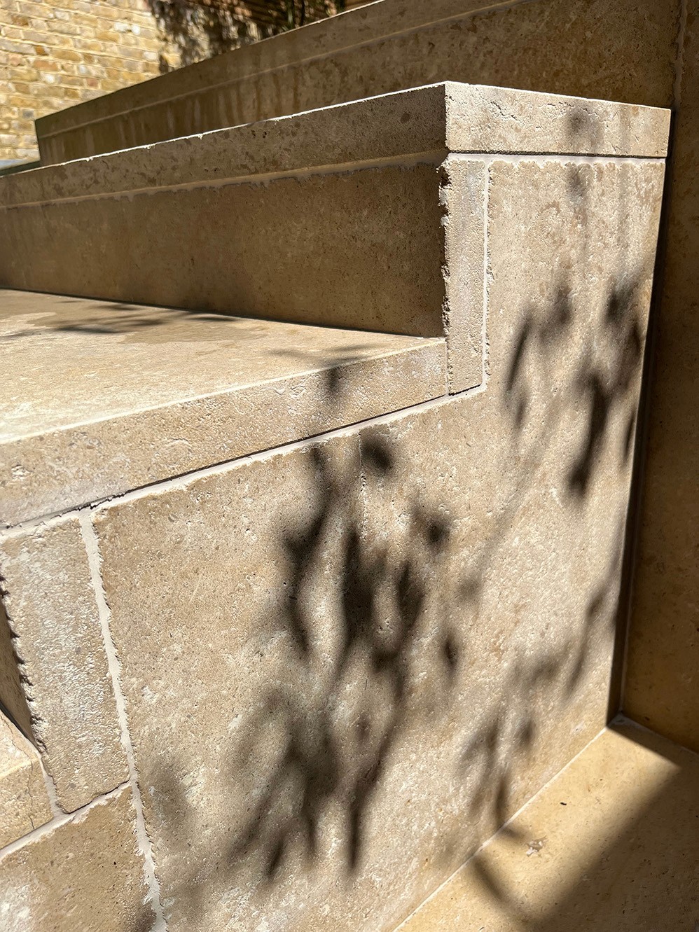 Close-up of a stone step, featuring intricate carvings and shadows cast by nearby foliage.