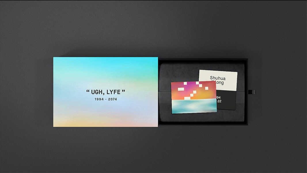 The image shows a black box open on a dark gray surface, revealing two cards inside. The larger card on the left has a gradient background transitioning from blue at the top to yellow at the bottom, with “UGH, LYFE” written in black text and the years “1994 - 2074” below. The smaller card on the right is white with black text reading “Shuhua Wrong”. The box is slightly ajar, revealing the cards and text within.